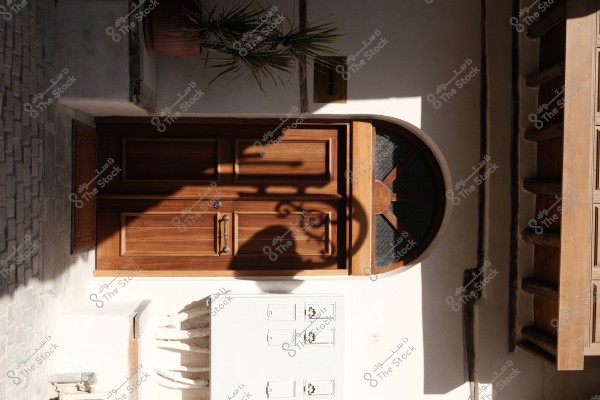 باب خشبي بني مع نافذة نصف دائرية، وظلال شمسية على الجدار المجاور