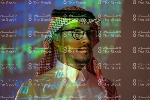 شاب سعودي يرتدي الزي السعودي التقليدي يتابع سوق الأسهم ويظهر انعكاس أضواء الشاشة عليه, رجل يتابع سوق المال