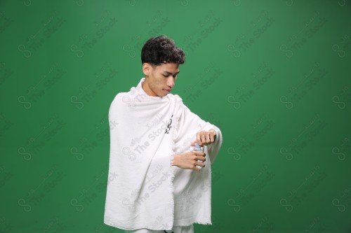 Portrait of a pilgrim with white skin on a green background wearing Ihram drinking water in several directions