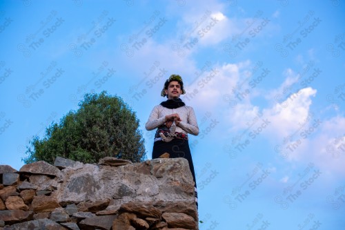 A Saudi man wearing a traditional dress at the top of the mountain and behind him clouds appear in Jizan