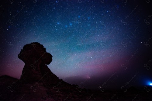 A night shot of a group of mountains in the deserts of Saudi Arabia, showing a clear sky sparkling with stars and planets at night in the middle of the desert