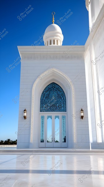 An image showing the facade of a mosque with a beautiful white dome adorned with golden decorations and a large door with blue stained glass. The architecture features white tiles and intricately decorated arches, with traditional lanterns enhancing the scene. The clear blue sky adds to the splendor of the exterior view.