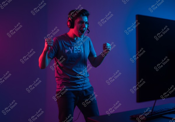 An image of a person wearing headphones and a t-shirt with \"YES!\" written on it, set in neon lighting with blue and red hues. The person looks excited, with their fists raised in the air, standing in front of a large screen, possibly during gaming or watching something thrilling.