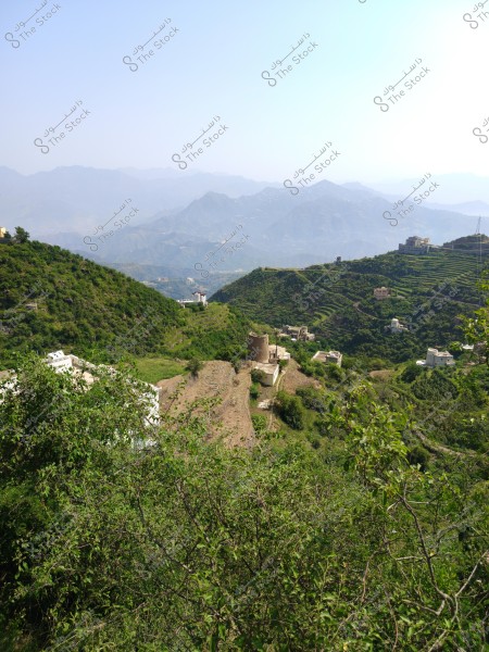 A natural landscape of terraced green mountains in Saudi Arabia. The hills are covered with dense vegetation, and traditional buildings are scattered across the mountain slopes. In the background, a range of mountains stretches to the horizon under a clear blue sky.