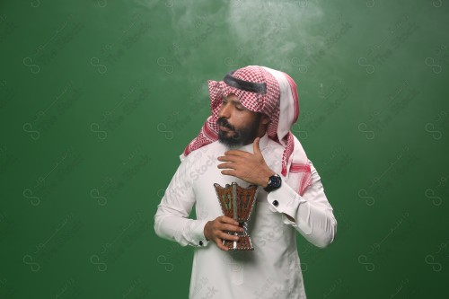 بورتريه رجل سعودي يرتدي الزي السعودي التقليدي يحمل المبخرة ويتطيب بالبخور