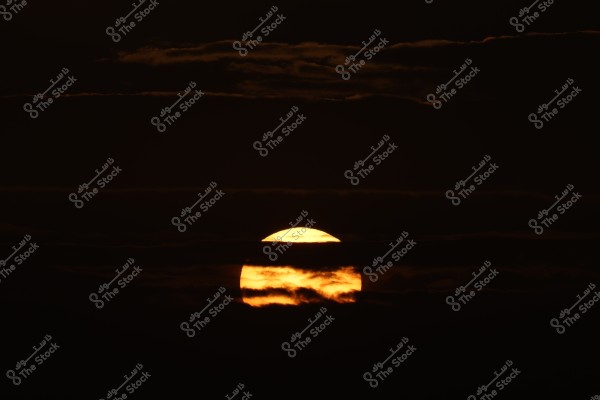 An image of the setting sun partially covered by dark clouds. The surrounding sky is dark, highlighting the prominent golden light of the sun.