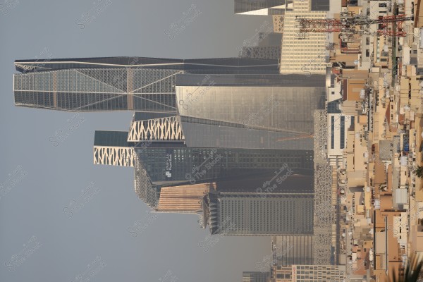 The image shows a cityscape during the day with a cluster of modern skyscrapers in the background. The buildings feature unique architectural designs and glass facades, highlighting the urban skyline. A communication antenna is visible in the foreground to the right.