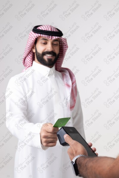 Portrait of a Saudi man holding a card and making automatic payments on a white background