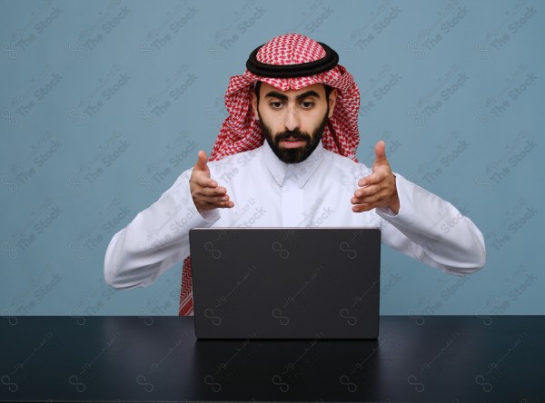 بورتريه شاب سعودي يرتدي الزي السعودي يستخدم جهاز المحمول ويتفاعل معه ، يقف على خلفية سماوية.