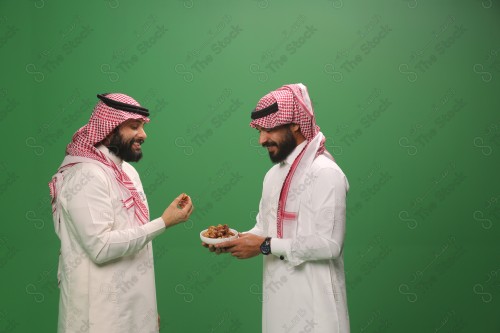 رجل سعودي يرتدي الزي السعودي التقليدي يقدم طبق من التمر لضيفه في أحد المناسبات