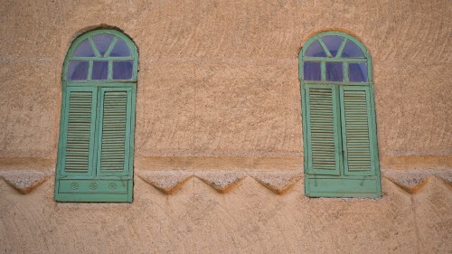 A mud building with a set of windows in the middle during the day