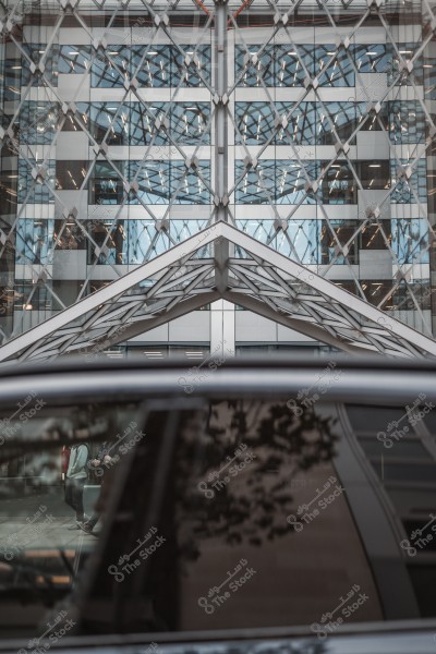 A modern glass building with a complex geometric design reflecting lights, with a car in the foreground.