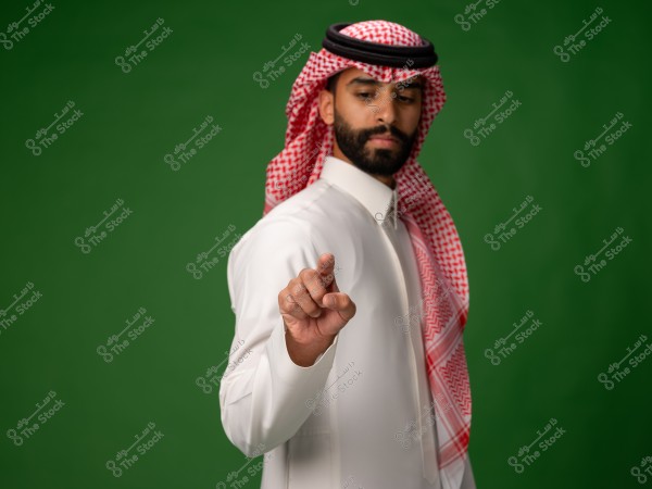 رجل يرتدي الزي التقليدي السعودي يقف أمام خلفية خضراء ويشير بإصبعه إلى الأمام.
