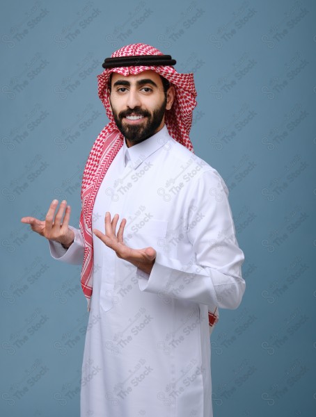 بورتريه شاب سعودي يرتدي الزي السعودي يقوم بالتفاعل بيدية ، ويظهر بتعابير وجه، على خلفية سماويه