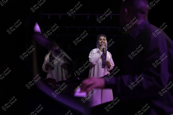 امرأة تغني على المسرح بينما يعزف رجل البيانو في المقدمة.