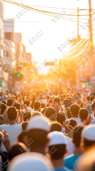 Image of a large crowd of people walking down a street under intense sunlight, creating a warm ambiance. The crowd has their hands raised or are walking together amidst surrounding buildings.