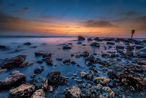 A shot of a group of coral rocks at Al Khobar Corniche at sunset, showing the sky in orange, the Arabian Gulf Sea.