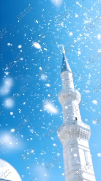 The image shows a minaret rising into a clear blue sky, with scattered light spots or droplets adding movement and depth to the scene. The minaret is white, displaying clear architectural details indicative of traditional Islamic design.