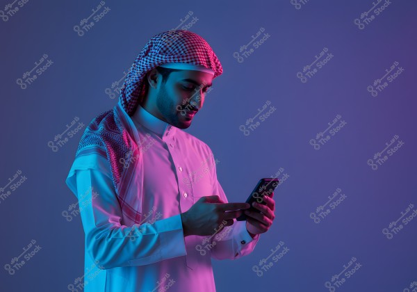 A portrait of a man wearing a white thobe and a red ghutra, likely from the Gulf region, looking at his smartphone with blue and violet lighting reflecting on him.