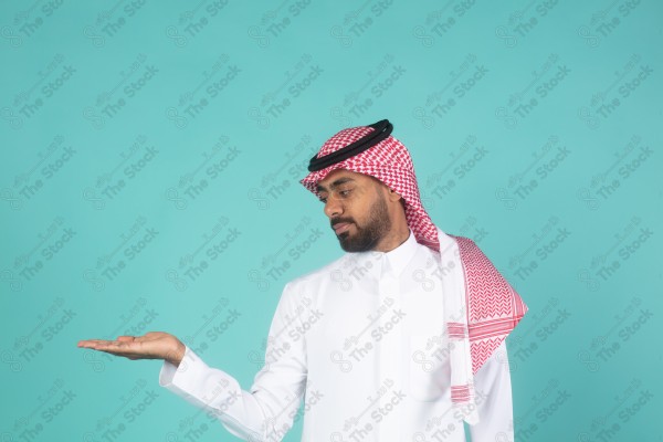 بورتريه رجل سعودي يرتدي الثوب ويقف أمام خلفية تركوازي ، يتفاعل بإشارات تعبيرية بيديه