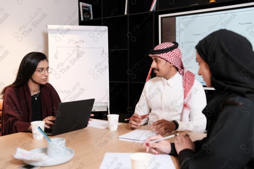 A Saudi man in traditional Saudi dress holds a meeting with Saudi female employees wearing abaya in the meeting room