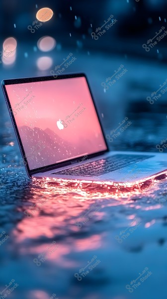 An image of an open laptop with a glowing pink screen, caught in the rain. Raindrops are visible on the screen and keyboard, with light reflections on the surrounding water creating colorful light effects.