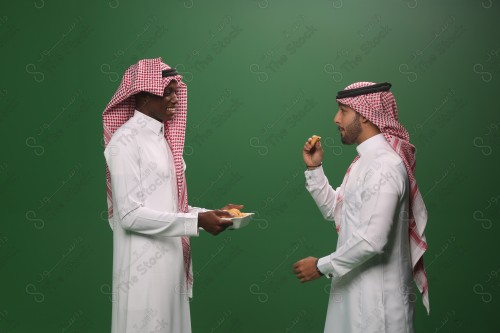 رجل سعودي يرتدي الزي السعودي التقليدي يقدم لضيفه طبق المعمول في إحدى المناسبات