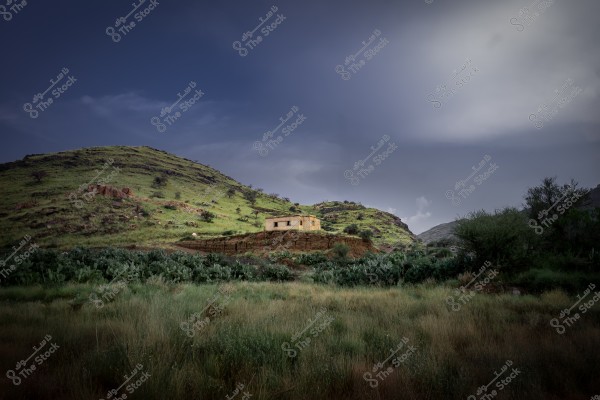 A small house on top of a hill in a mountainous landscape with a dark sky in the background.