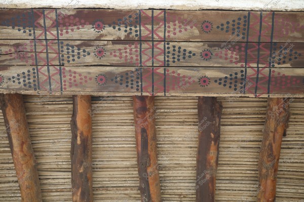 An image showing a traditional wooden ceiling with wooden beams, featuring decorative designs with circular patterns and dots colored in red, blue, and black.