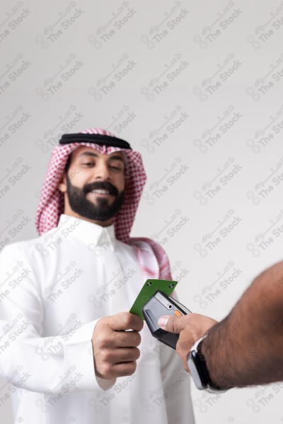 Portrait of a Saudi man holding a card and making automatic payments on a white background