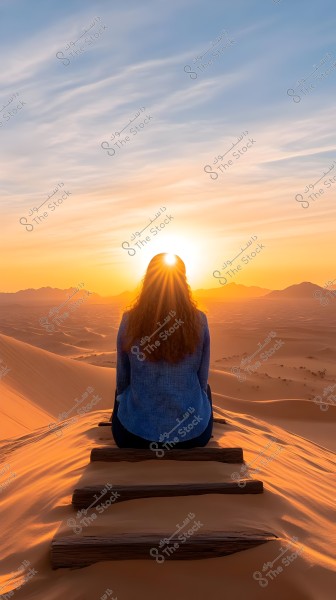 An image of a person sitting on a sand-covered wooden staircase, watching the sunset in the desert. The person is wearing a blue sweater and appears tranquil while contemplating the surrounding natural scenery, with the sun\'s rays reflecting on the golden sand dunes in the vast horizon.