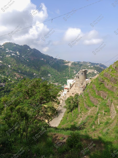 A landscape view of a lush green mountainous area featuring agricultural terraces in the foreground and traditional buildings on the mountain slope. Small villages appear scattered across the hills in the distance under a blue sky with some clouds.