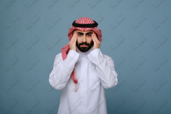 بورتريه شاب سعودي يرتدي الزي السعودي على خلفية سماوية، يمسك رأسه ، يشعر بالصداع ،آلام الصداع والمرض