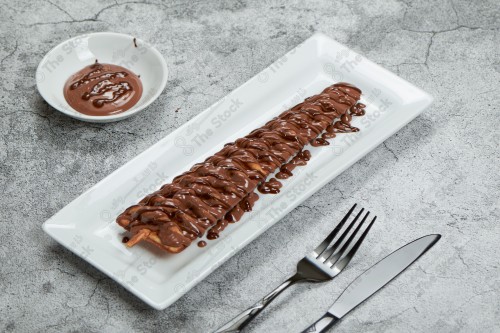 Close-up of a waffle plate covered in chocolate sauce on a white background with fork and knife, sweets.