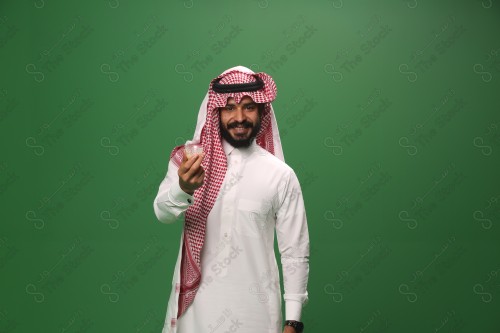 شاب سعودي على خلفية خضراء يرتدي الثوب و الشماغ، يقوم بعمل حركات بيده، يشرب القهوه السعودية، احتفالات العيد