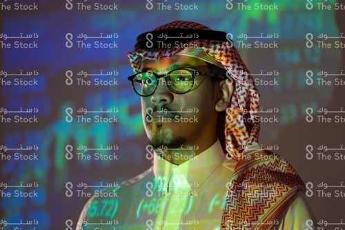 شاب سعودي يرتدي الزي السعودي التقليدي يتابع سوق الأسهم ويظهر انعكاس أضواء الشاشة عليه, رجل يتابع سوق المال