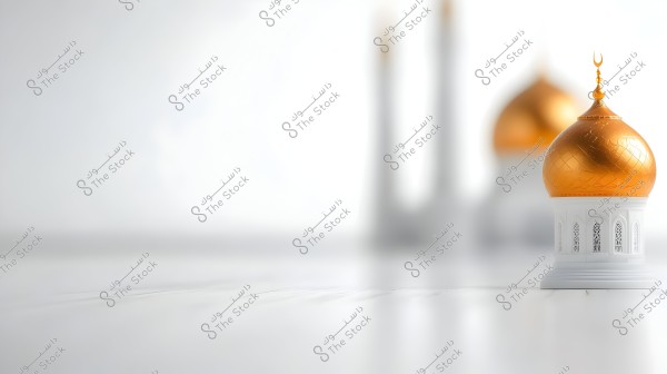 The image features a model of a mosque with Islamic design. The model has a golden dome situated on a white base adorned with arched windows. The background is blurry, containing similar elements of the mosque design, giving a sense of depth and tranquility.