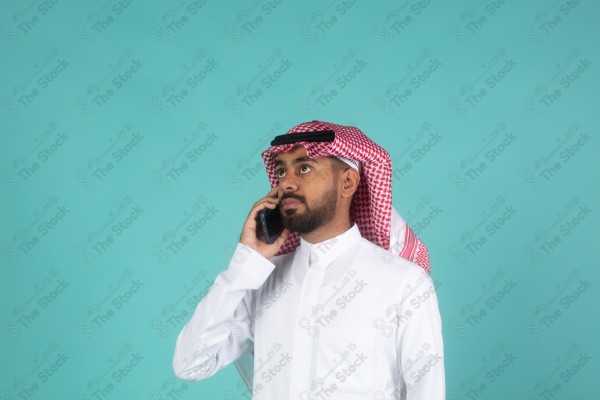 بورتريه رجل سعودي على خلفية تركوازي،  يرتدي الزي السعودي التقليدي يتحدث بهاتفه، الاتصالات والتقنية