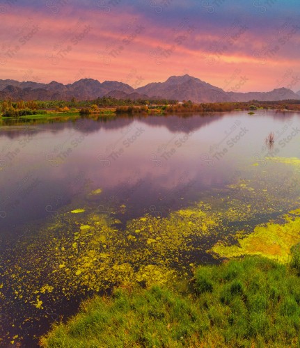 An overhead shot of a series of rocky mountains with a pond in the middle of it in Wadi Al-Bayda / Wadi Al-Jin, showing the sky is cloudy during the day.