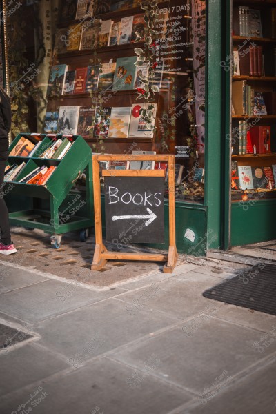 Image of a bookstore with a glass window display filled with books. There is a wooden sign with the word \"Books\" and an arrow pointing inside.