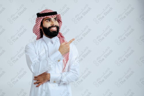 بورتريه رجل سعودي يرتدي الزي الرسمي التقليدي على خلفية بيضاء يقوم بعمل اشارات بيديه وهو مبتسم ، صور تذكارية ، توثيق لحظة سعيدة.