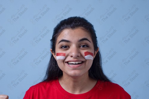 Portrait of a Saudi woman wearing a red T-shirt cheering the football team on a blue background and showing expressions of joy and enthusiasm, World Cup.