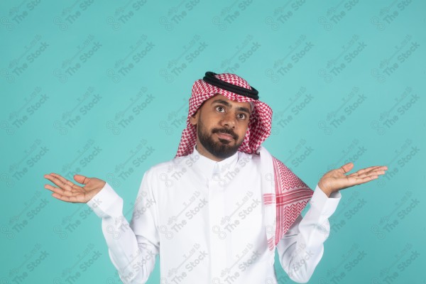 شاب سعودي على خلفية تركوازيه يعمل اشارات بيده ، تبدوا على ملامحه التعجب والاستغراب، ثوب وشماغ