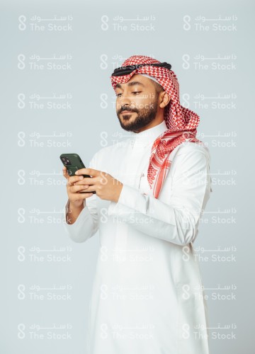 بورتريه رجل سعودي يرتدي الزي السعودي التقليدي يستخدم الجوال وينظر للشاشة بينما يتصفحه