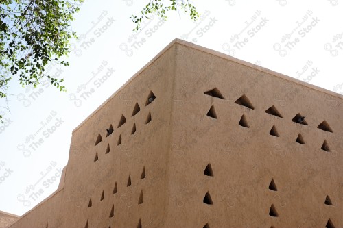 A heritage building built of mud in the middle of it, a group of holes in the Najd style, and the sky appears clear during the day