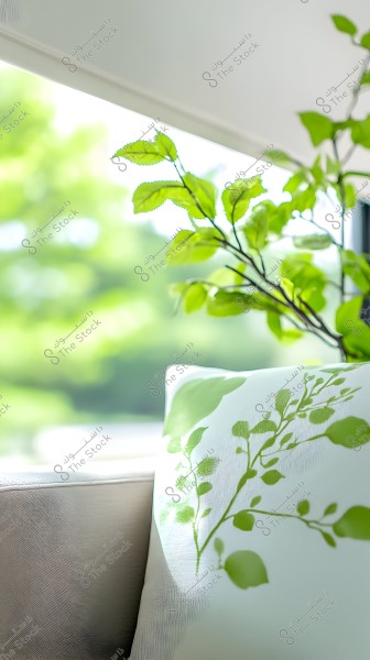 An image focusing on a white pillow with green leaf-like patterns on it. Next to the pillow, there are branches of a plant with vibrant green leaves. In the background, there is a scene that appears to be a sunlit green garden.