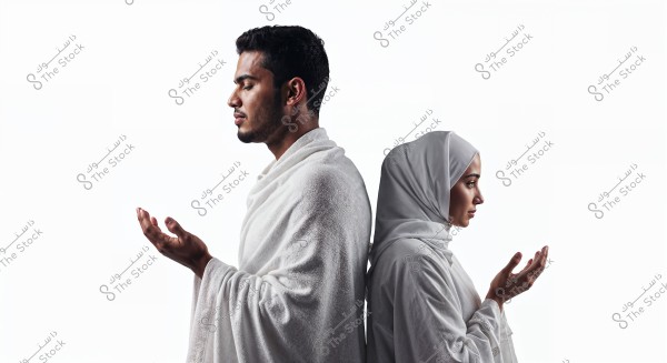An image of a man and a woman standing back-to-back, both dressed in white attire. The man wears an Ihram, suggesting that he might be in the context of Hajj or Umrah, while the woman is wearing a white hijab. Both are in a prayer position, indicating a moment of contemplation and prayer.\r\n\r\n###