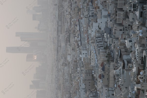 An image of a city skyline showing Riyadh in Saudi Arabia. Several skyscrapers are visible in the background, while residential buildings fill the horizon in the foreground. The sky appears gray with a soft sunlight indicating that it is near sunset.