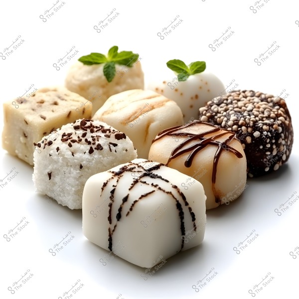 A variety of square-shaped desserts arranged on a white plate. The sweets feature different layers and flavors, some drizzled with liquid chocolate, others coated with sprinkles and garnished with green mint leaves. The assortment showcases diversity and elegance.