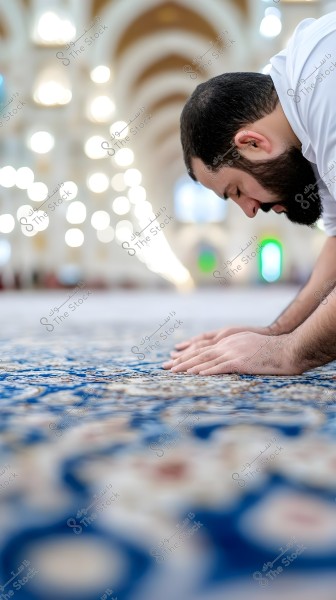 رجل يقوم بالصلاة داخل مسجد, وهو في وضع السجود على سجادة زرقاء مزخرفة. في الخلفية تظهر العديد من الأضواء المبهرة والأقواس المعمارية التي تضيف جمالاً وروحانية للمكان.